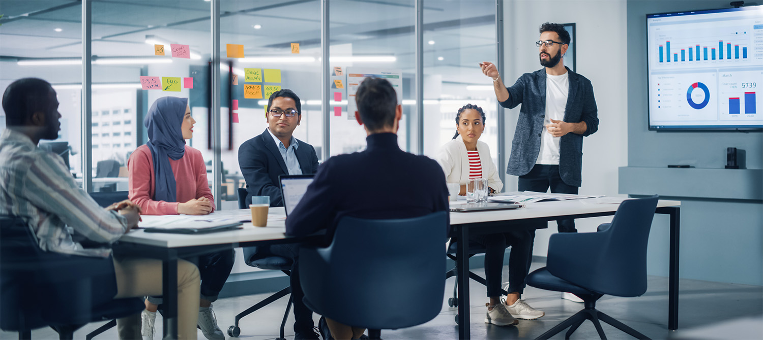 Meeting room with a diverse group of people talking and looking at business graph on a display monitor