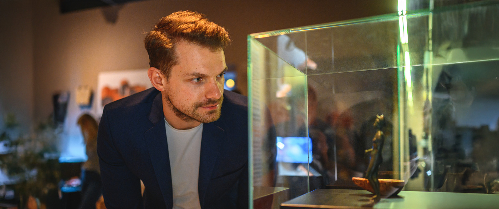 Man at a museum looking into a display case housing a small ancient statue.